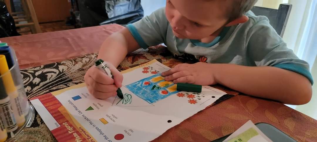 a young student colors in a math worksheet at their desk