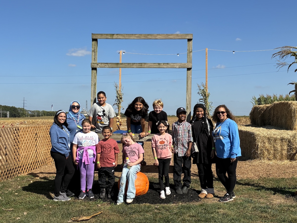 A group of students and their families pose in a corn field at a pumpkin patch.
