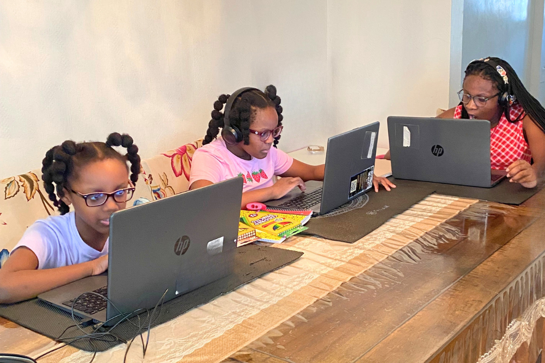 Three students sit around their dining room table working on lap tops